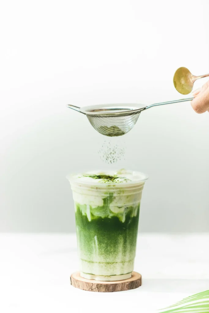 Matcha Latte im durchsichtigen Becher mit Schichten aus grüner Teebasis und weißer Milch, bestreut mit Matcha-Pulver